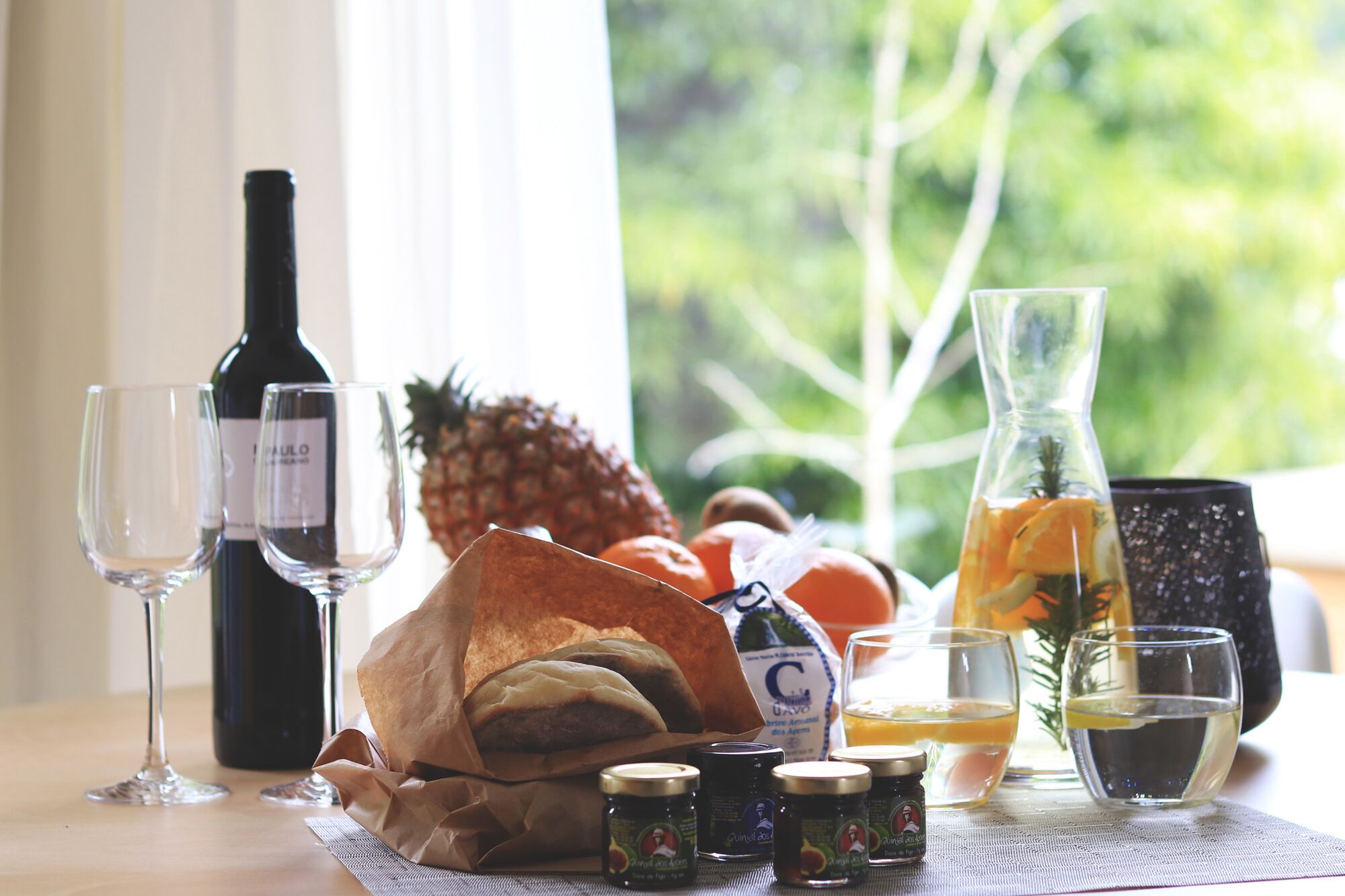 Een tafel met wijn, glazen, een belegd broodje, fruit, een karaf en bijgerechten.
