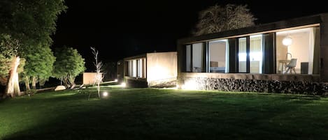 Un bâtiment moderne doté de grandes fenêtres et d’un socle en pierre, entouré d’une pelouse bien entretenue et d’arbres.