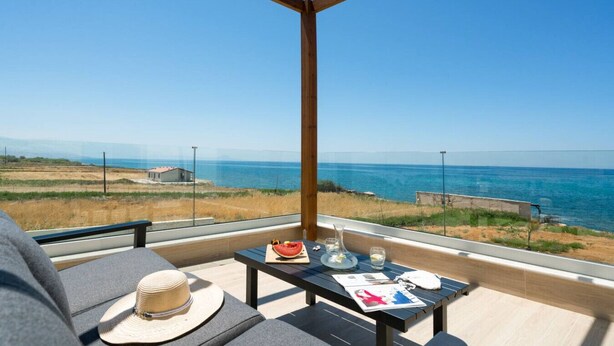A balcony with a view of the sea, a table with a hat, a watermelon, and glasses.