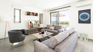 A modern living room with a large window, a flat-screen TV, a grey sofa, a coffee table, and a side table.