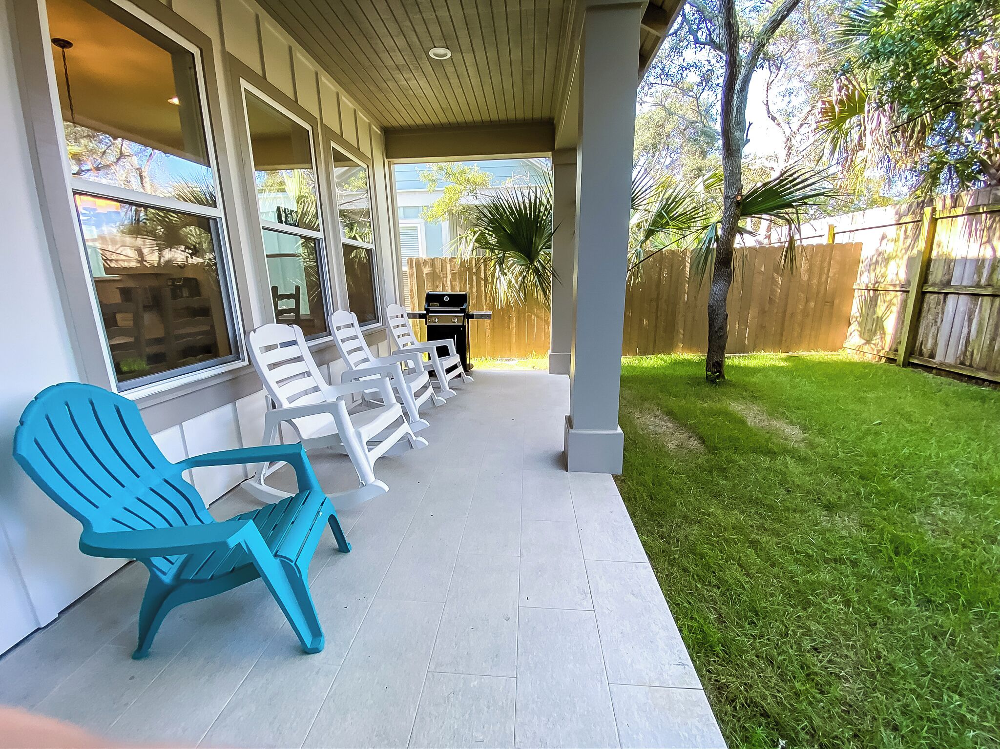 Een overdekt terras met witte loungestoelen, een blauwe stoel en een barbecue.