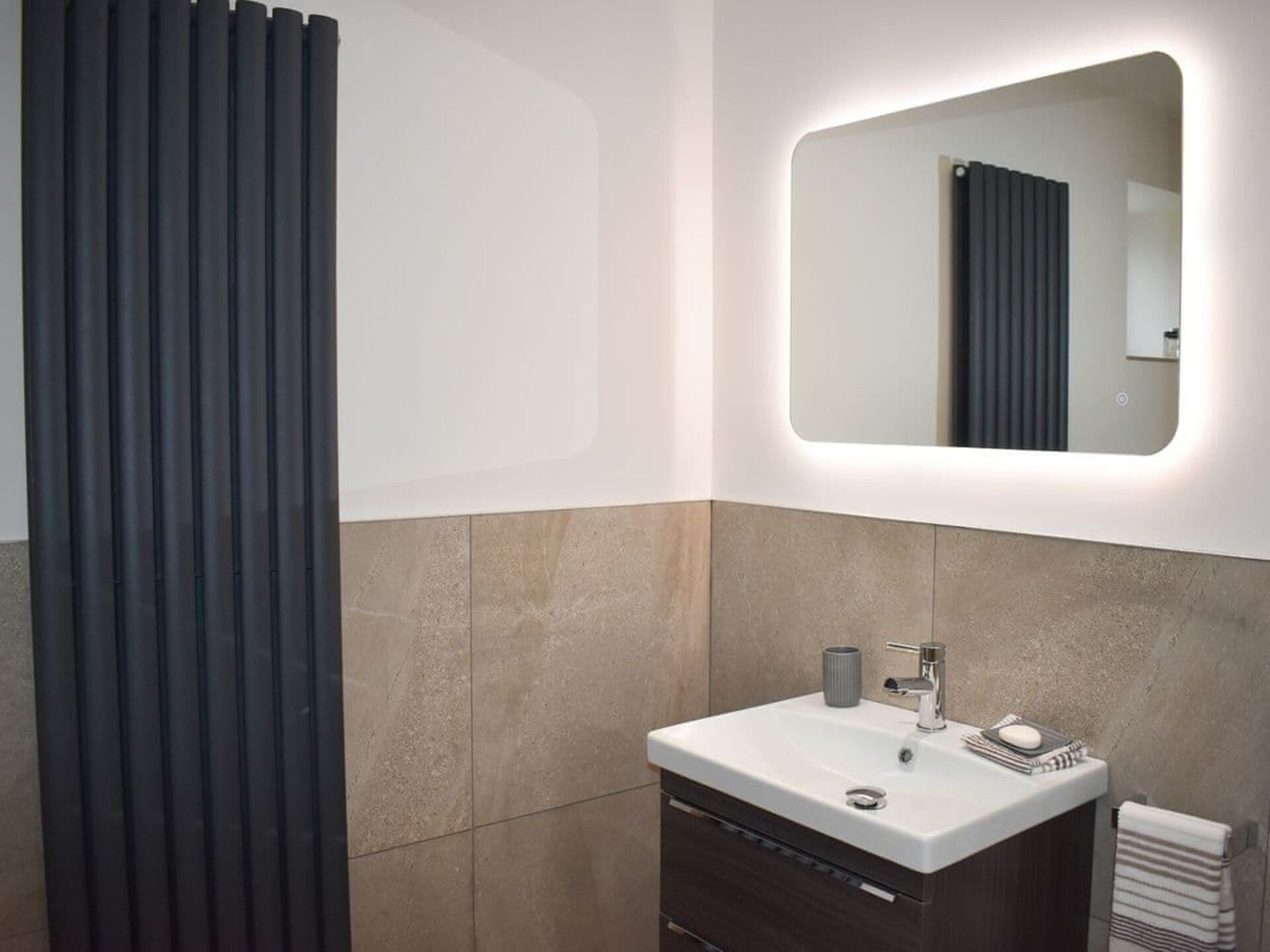A modern bathroom with a white sink, dark wooden cabinet, and a mirror with a lighted frame.