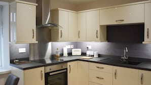 Una cocina moderna con gabinetes color beige, encimera negra, campana extractora de acero inoxidable, horno empotrado y un fregadero.