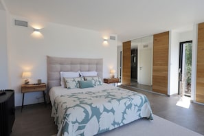 Une chambre à coucher moderne avec un grand lit, des tables de chevet, un miroir et une vue sur l’extérieur.