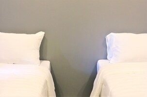 Dos camas individuales con ropa de cama blanca frente a una pared gris.