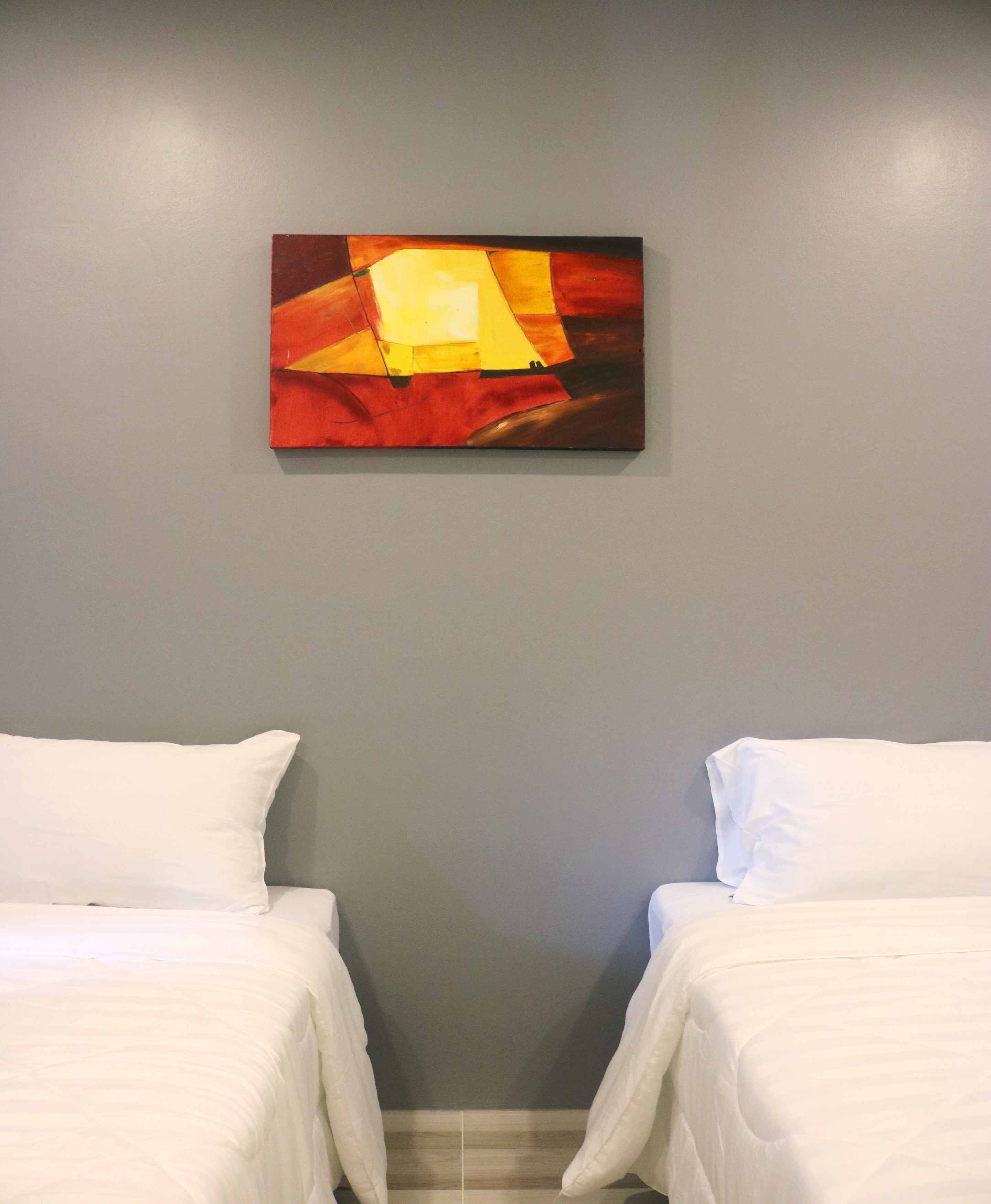 A hotel room with two beds, a gray wall, and a painting above the beds.