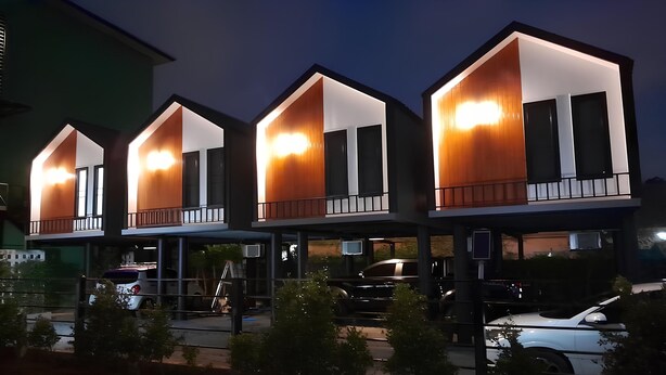 Une rangée d’immeubles modernes à plusieurs étages, dotés de balcons illuminés et de grandes fenêtres.