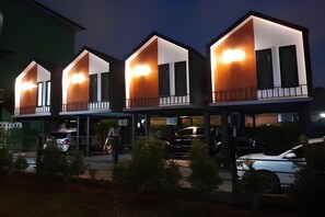 A row of modern, multi-story buildings with illuminated balconies and large windows.