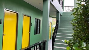 Un couloir aux murs verts et aux portes jaunes, qui mène à un escalier.