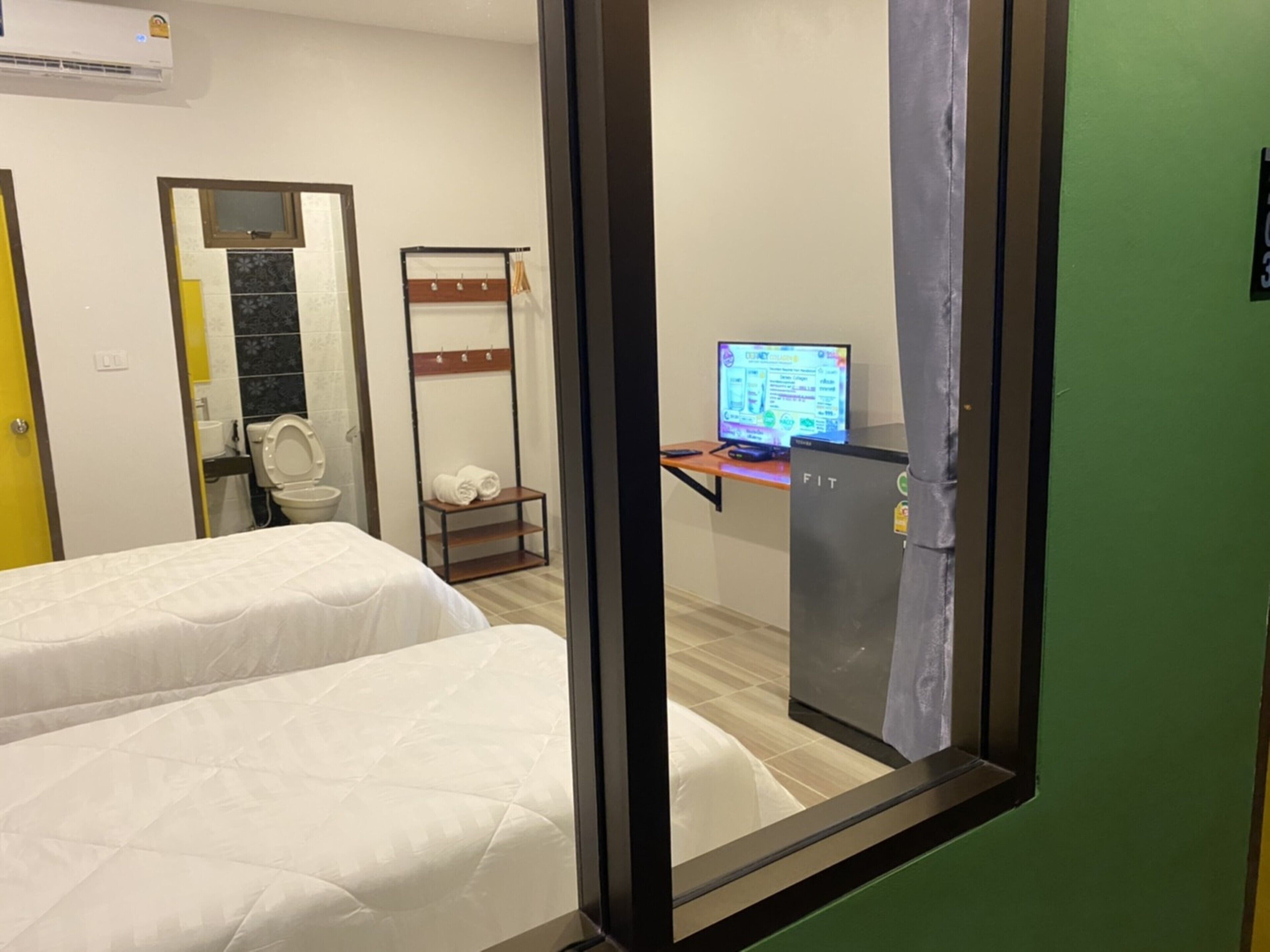 Habitación de hotel con dos camas, un escritorio con ordenador, un inodoro y un estante con toallas.