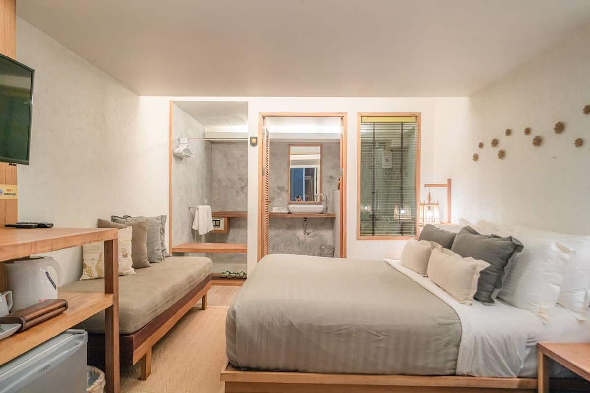 A modern hotel room with a large bed, a desk with a kettle, a small table, and a TV.