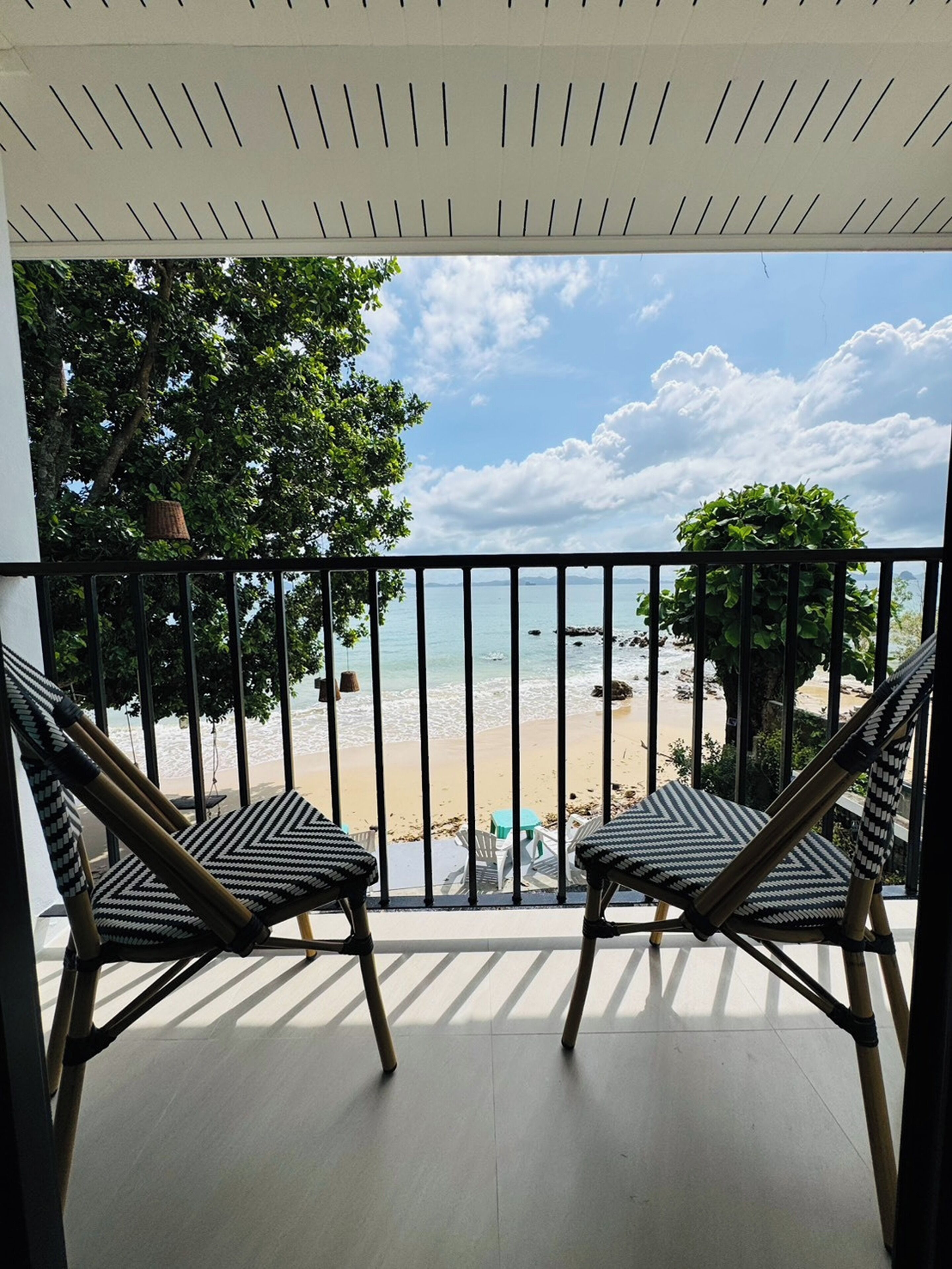 Ein Balkon mit zwei Stühlen und Blick auf einen Strand, bewölkter Himmel.