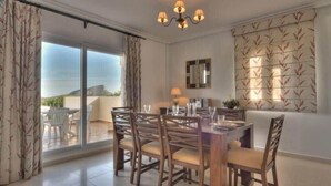 A dining area with a table set for four, a chandelier, and a view of the outdoors through a sliding glass door. - La Manga Club Monte Verde Villa 352 (La Manga Club, Cartagena)