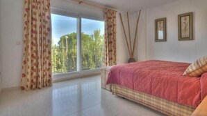 A bedroom with a large window, a bed with a red bedspread, and two framed pictures on the wall. - La Manga Club Monte Verde Villa 352 (La Manga Club, Cartagena)