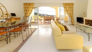 A modern living room with a sofa, dining table, and chairs. There is a TV and a fireplace.