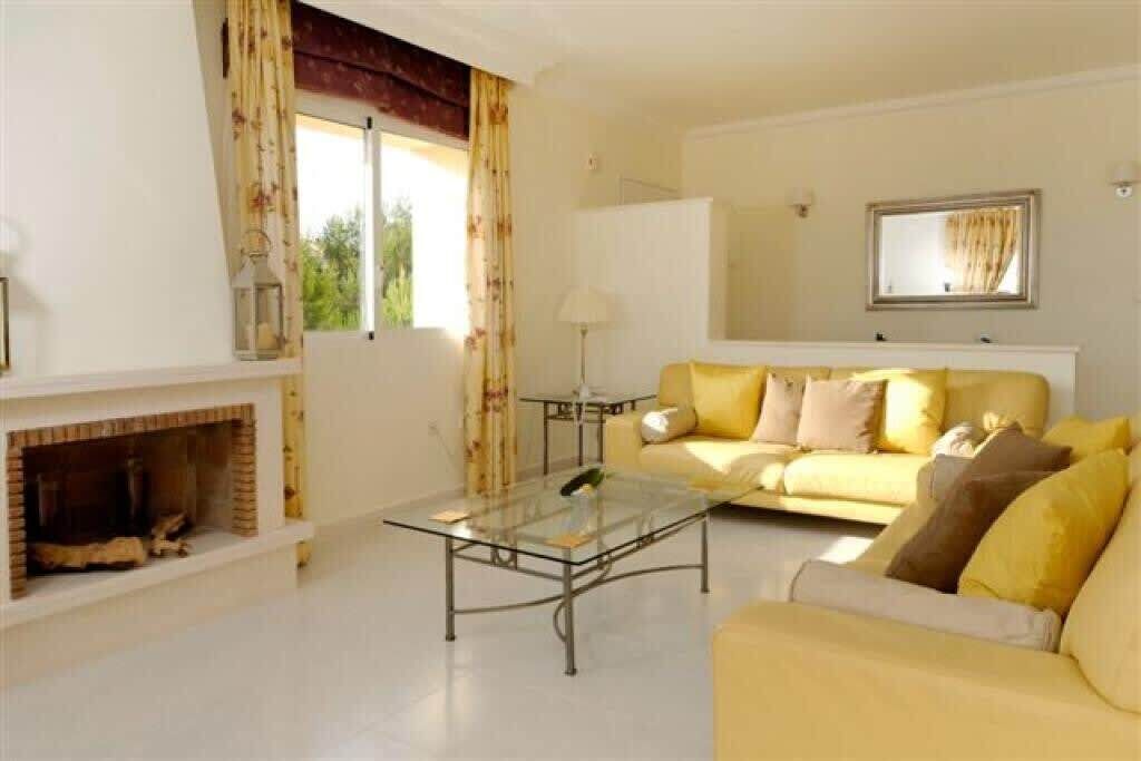 A living room with a sofa, a glass coffee table, a fireplace, and a window with curtains.