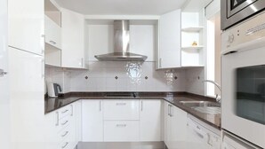 Una cocina moderna con armarios blancos, una campana extractora de acero inoxidable, horno empotrado y lavavajillas.