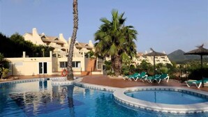 Una piscina con sillas de descanso, palmeras y edificios de un complejo turístico.