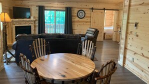 A cozy cabin interior with a wooden dining table, chairs, a sofa, and a fireplace. - Waterview Lodge Suite in Ohio's Amish Country (Millersburg)