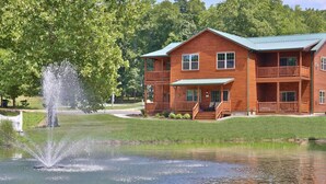 A two-story log cabin with a green roof, a front porch, and a pond with a fountain. - Waterview Lodge Suite in Ohio's Amish Country (Millersburg)