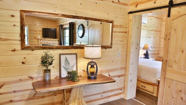 A wooden interior with a mirror, framed artwork, a lamp, and a small plant on a wooden table. - NEW Waterview Lodge Suite in Ohio's Amish Country (Millersburg)