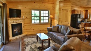 A cozy cabin interior with a fireplace, leather sofa, dining table, and kitchen area. - NEW Waterview Lodge Suite in Ohio's Amish Country (Millersburg)