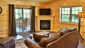 A log cabin interior with a fireplace, leather sofa, and a television. - NEW Waterview Lodge Suite in Ohio's Amish Country (Millersburg)