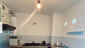 A compact kitchen with light blue cabinets, a wooden countertop, a built-in microwave, and a hanging light fixture. - T3 sea view apartment (Bastia)