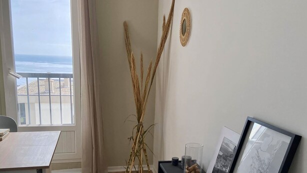 A room with a wooden floor, a dining table, a black console table with framed pictures, and a view of the sea through a window. - T3 sea view apartment (Bastia)