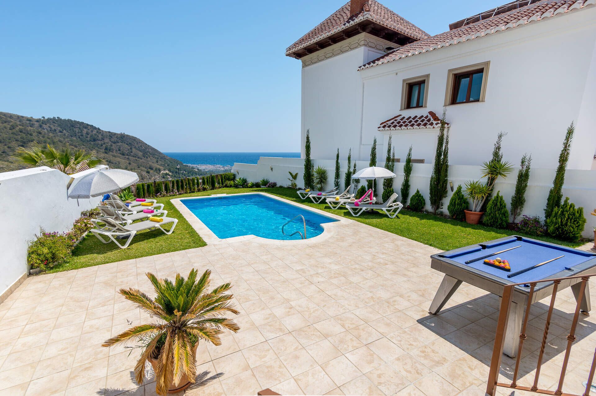 A pool area with a pool table, lounge chairs, and a view of the sea.