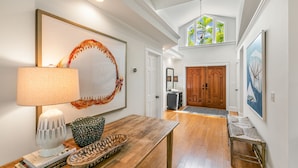 A spacious hallway with a wooden floor, a bench, a table with a lamp, and artwork on the walls. - SOUTHERN CROSS ~ Conveniently Located 3 Bedroom, 2.5 Bathroom Gem w/ Pool (Key West)