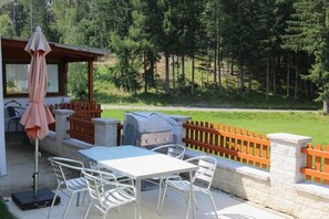 Um pátio externo com mesa, cadeiras, churrasqueira e cerca de madeira.