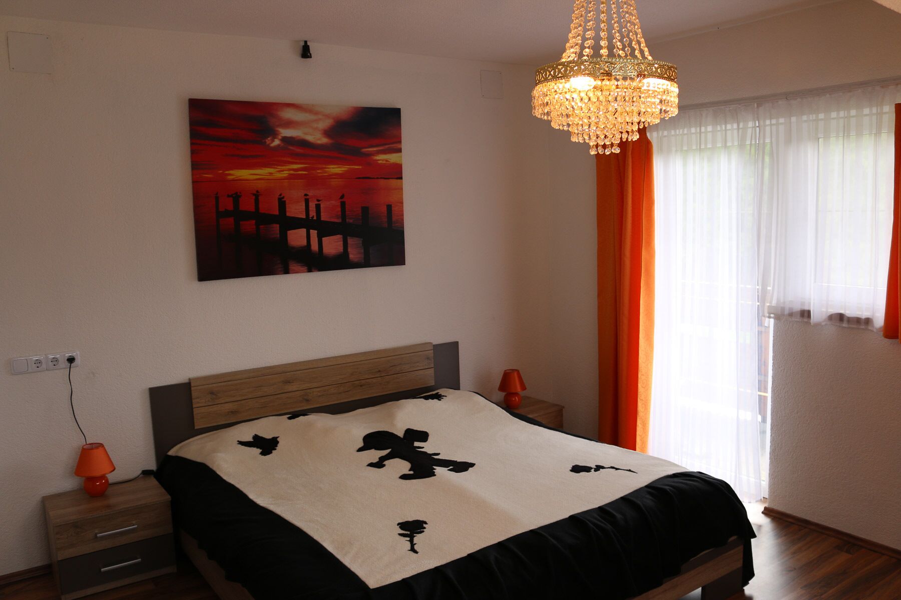 Une chambre à coucher avec un lit, une table de chevet, une lampe, un tableau et un lustre.