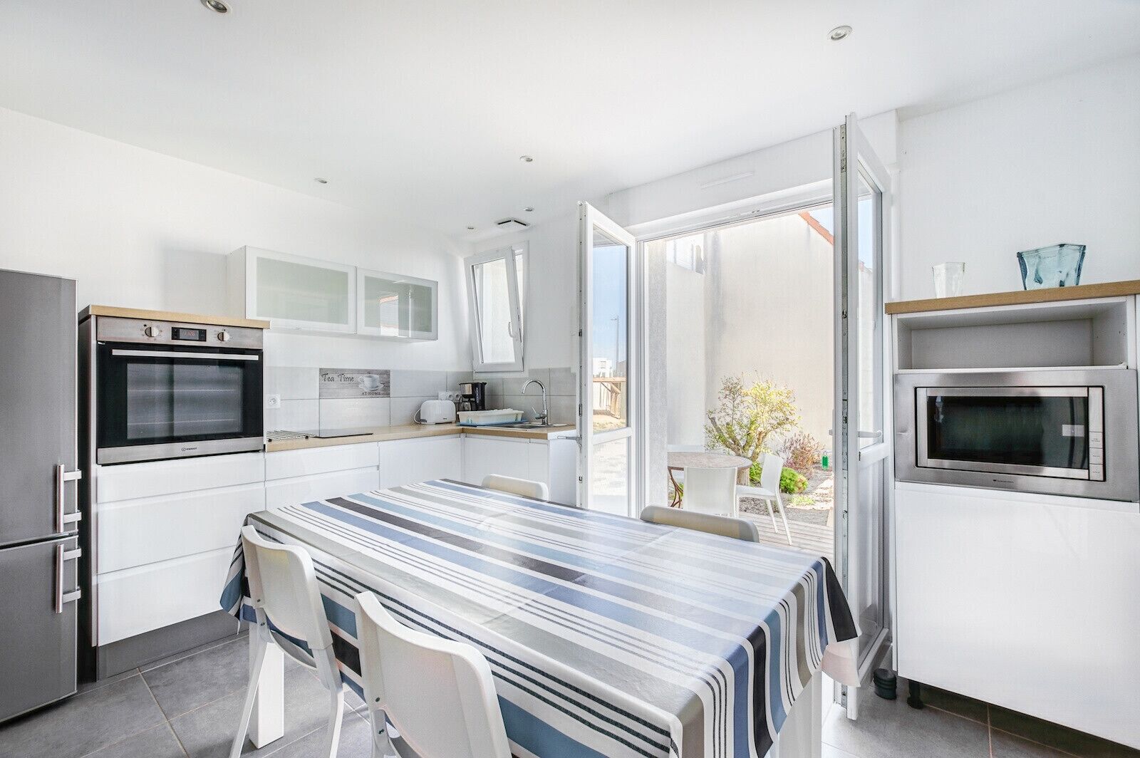 A modern kitchen with a large dining table, built-in appliances, and a view of the outdoors.