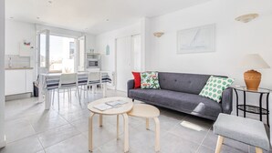 Una sala moderna con un sofá gris, una mesita redonda y un comedor con mantel a rayas.