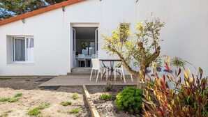 Una casa moderna con fachada blanca, una terraza de madera y un pequeño jardín con diversas plantas y flores.