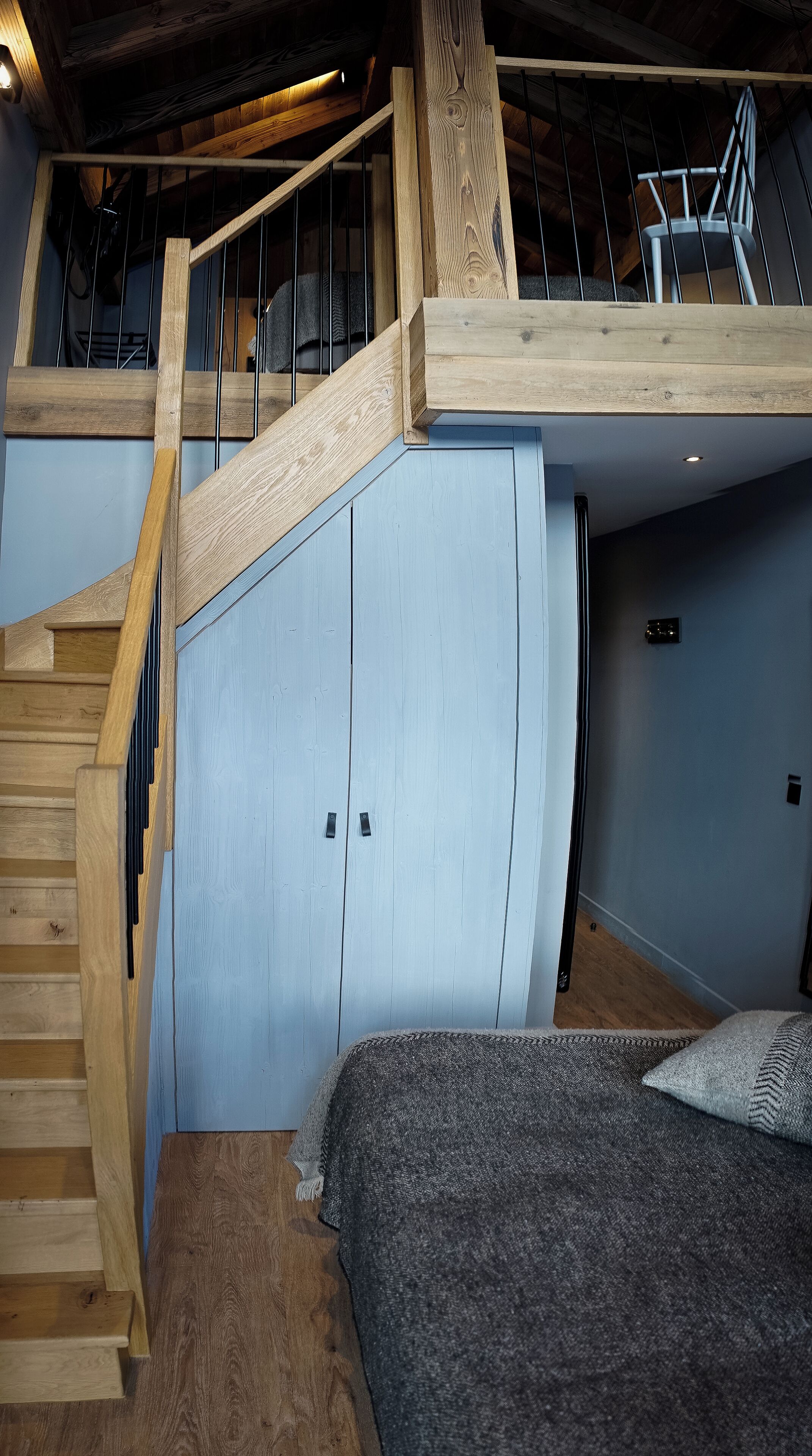 Une chambre de style loft avec un escalier en bois, un lit superposé et une mezzanine dotée d’une rambarde.