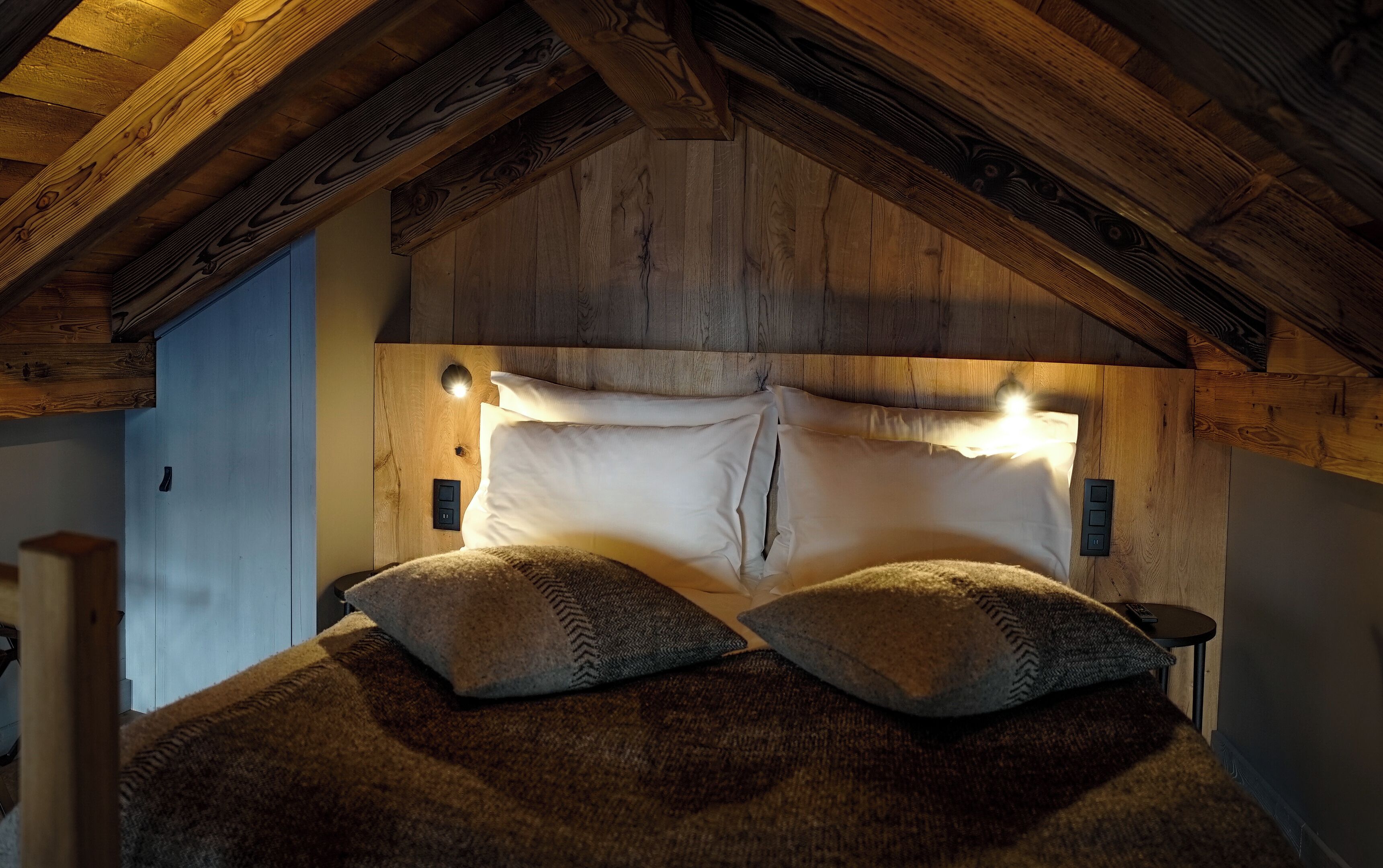 A cozy bedroom with a wooden ceiling, a bed with white linens, and two decorative pillows.