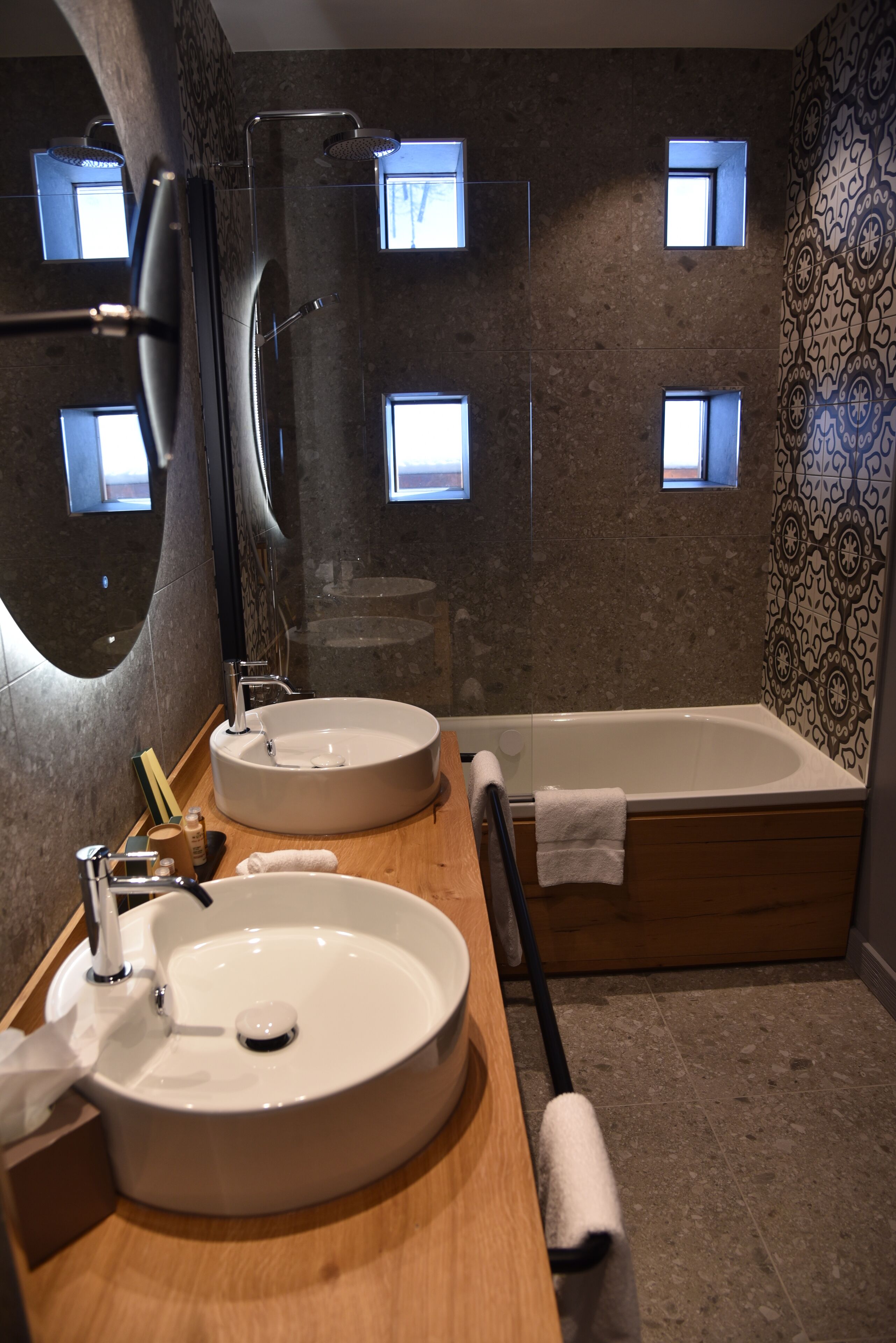A bathroom with two round sinks, a bathtub, and a large mirror.