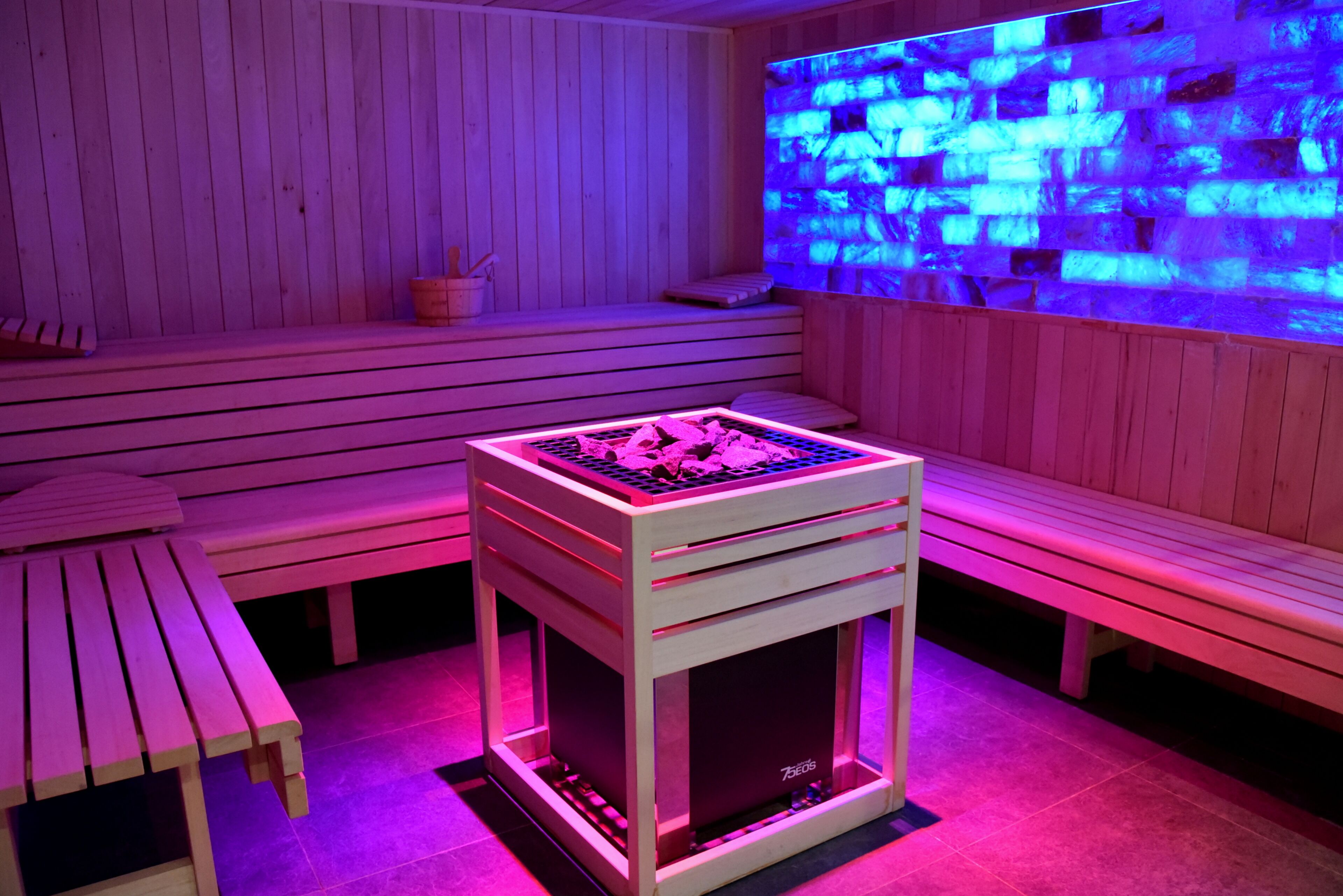 A wooden sauna room with benches, a massage table, and a massage table with a massage chair.