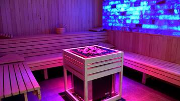 A wooden sauna room with benches, a massage table, and a massage table with a massage chair.