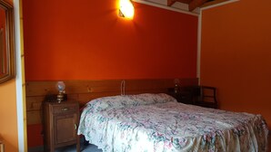 Quarto com cabeceira de madeira, colcha florida, mesa de cabeceira com abajur e luminária na parede.