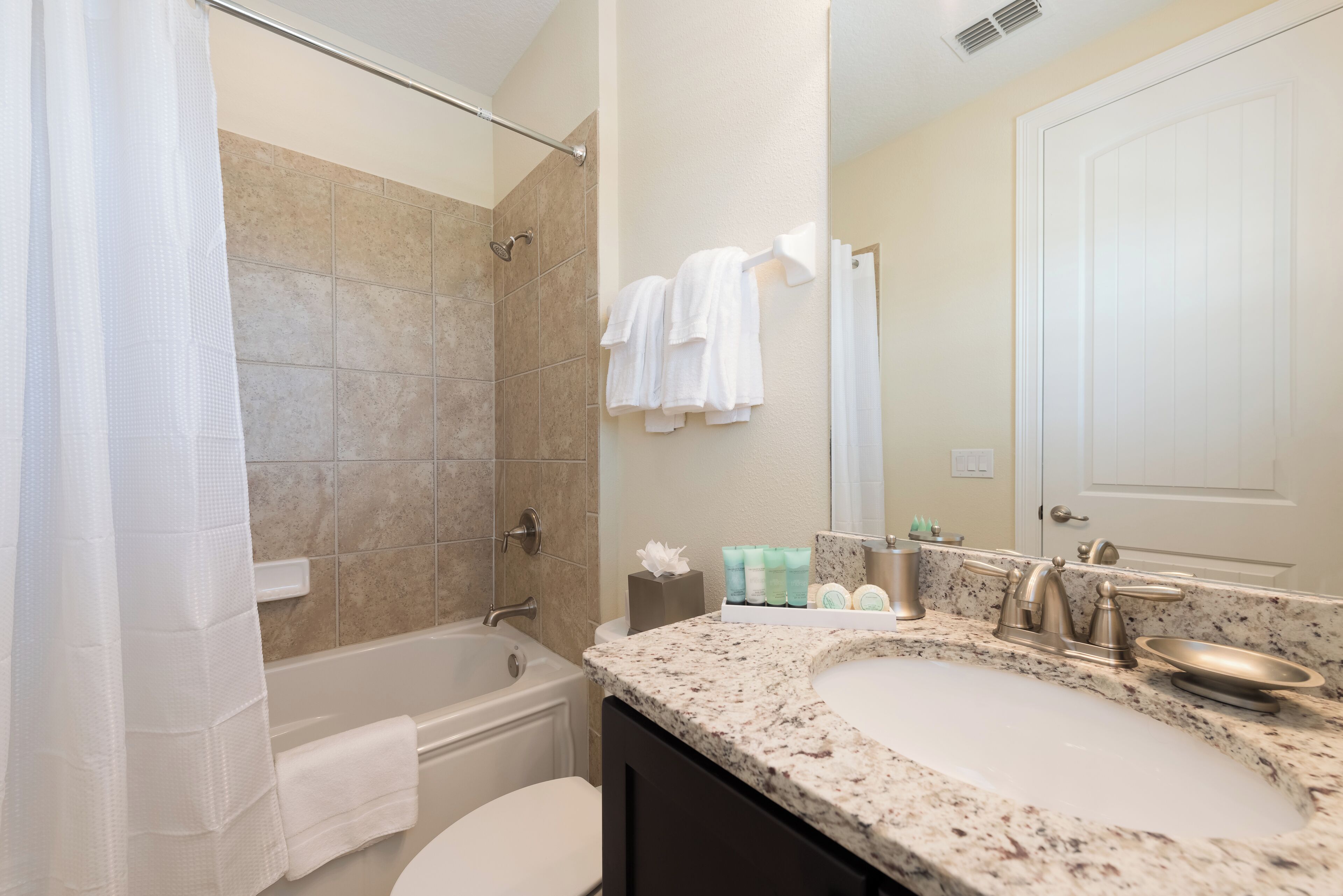 A bathroom with a bathtub, a sink, and a toilet. There are towels hanging on the wall and toiletries on the counter.