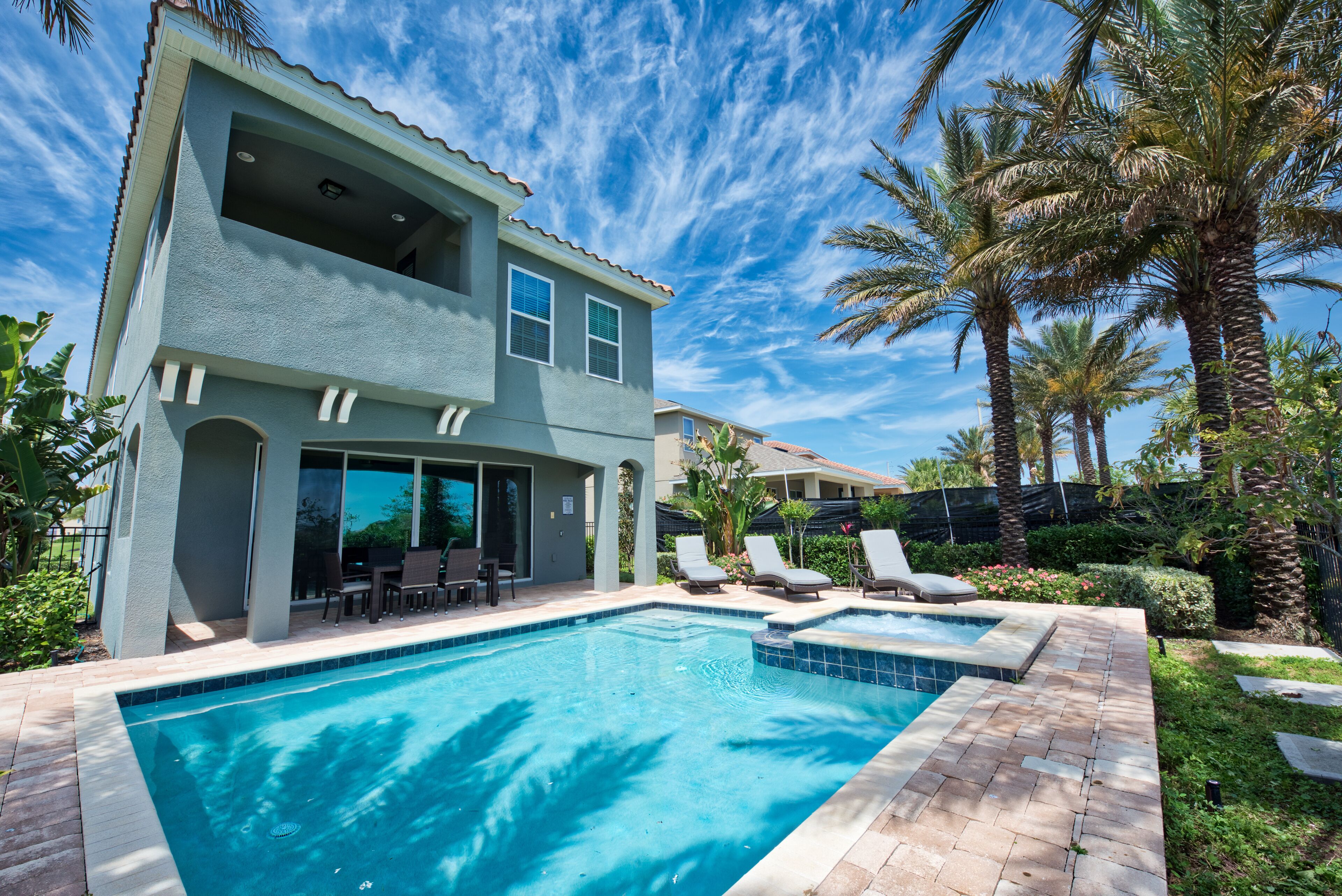 A two-story house with a swimming pool, outdoor seating, and palm trees.