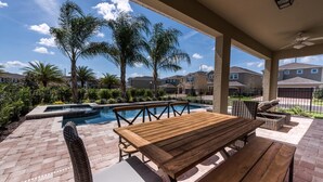 A patio with a wooden table and chairs, a pool, and a view of residential buildings.