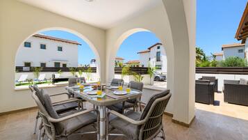 An outdoor dining area with wicker chairs and a table set for four, overlooking a pool and buildings.
