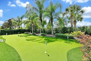 A well-maintained golf course with lush greenery, palm trees, and a clear sky.