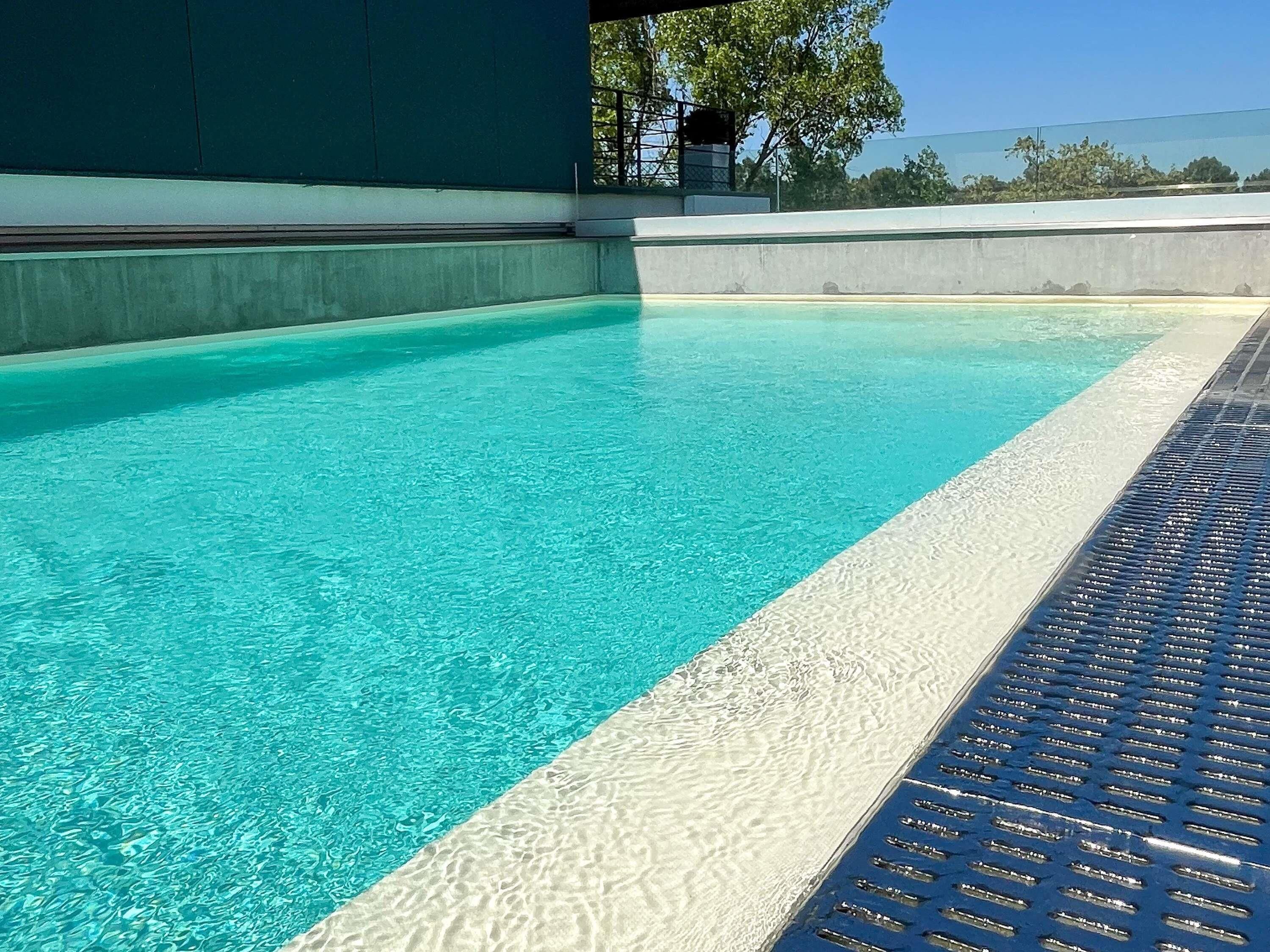 Une piscine aux eaux d’un bleu limpide, dotée d’un bord texturé et d’une barrière de sécurité en métal.