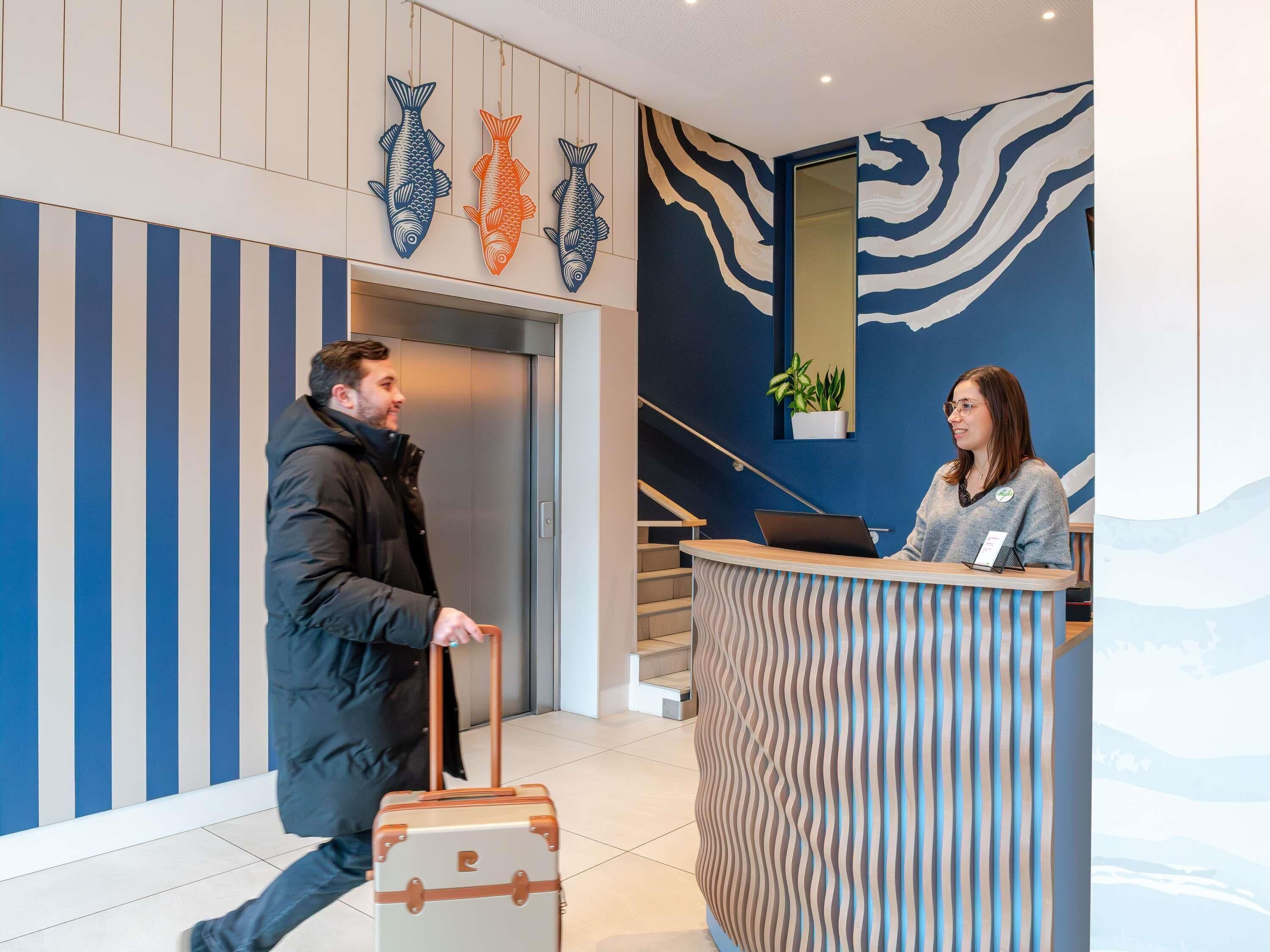 Zona de recepción de un hotel con diseño moderno, que incluye un mostrador de recepción, una escalera y decoración con arte de peces en la pared.
