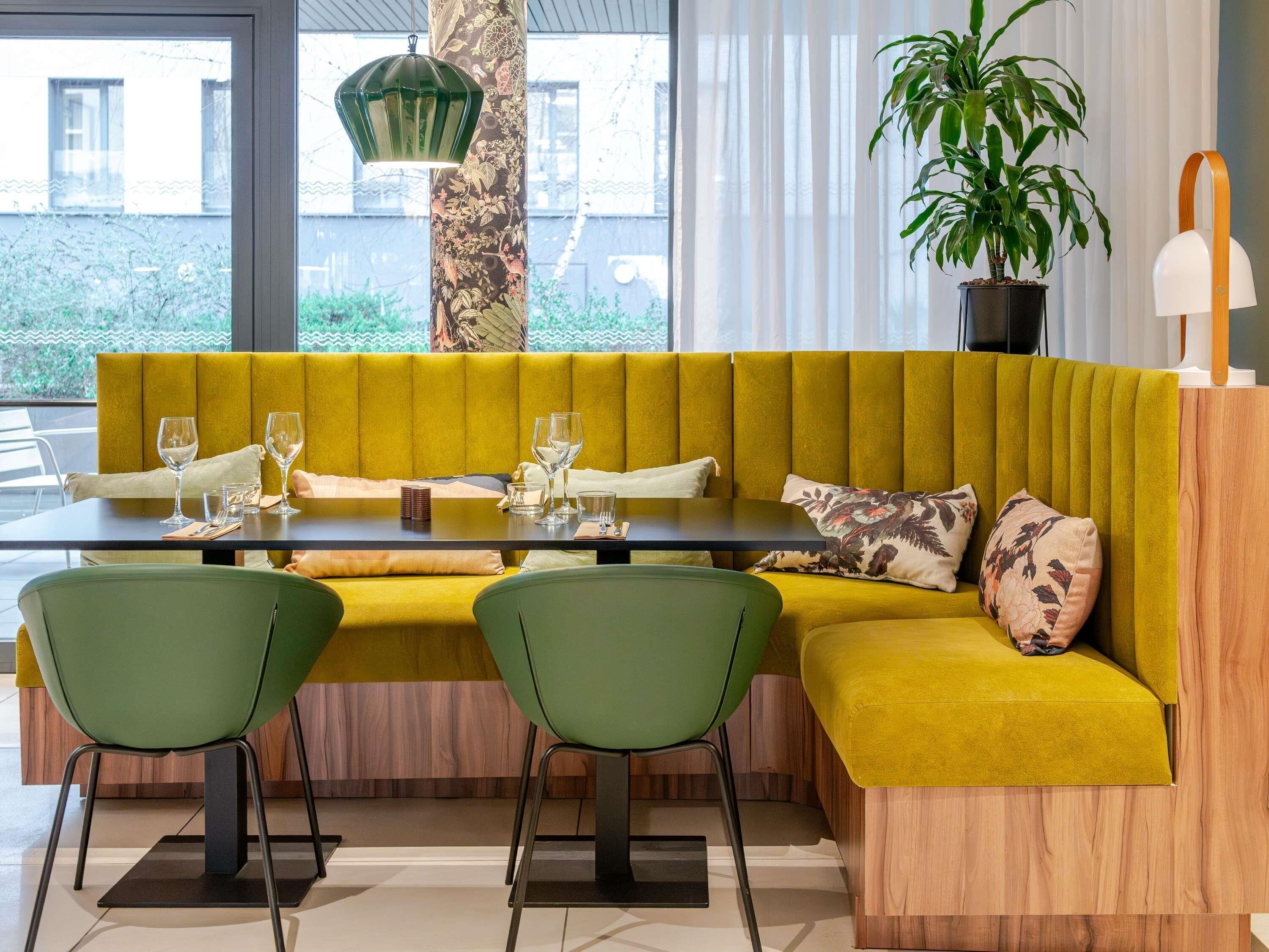 Un espace repas moderne avec un canapé jaune, des chaises vertes, une table en bois et une plante en pot.